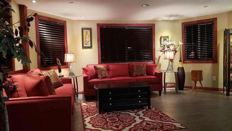 Main living room with red sofas and dark wood blinds on three windows