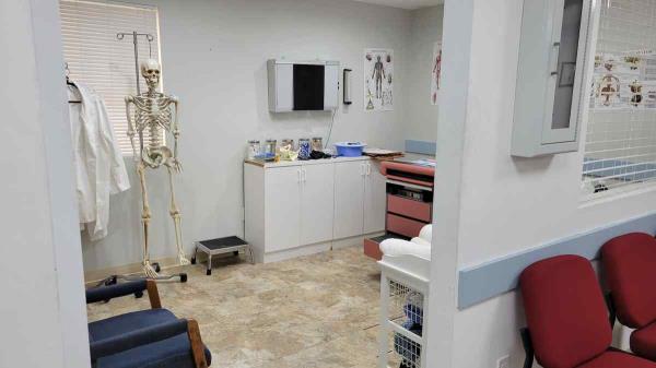 filming location hospital exam room with exam table, x-ray viewer, hospital props and hanging skeleton. View from adjecent hallway